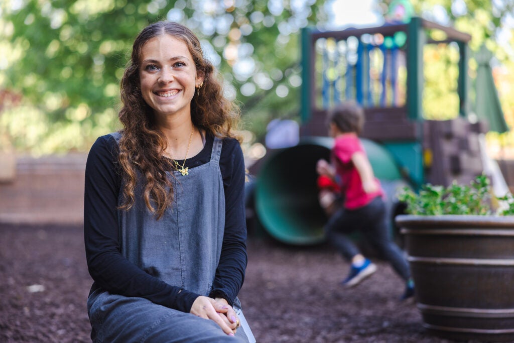 Abby Herring smiles at the camera while preschoolers play on the playground behind her