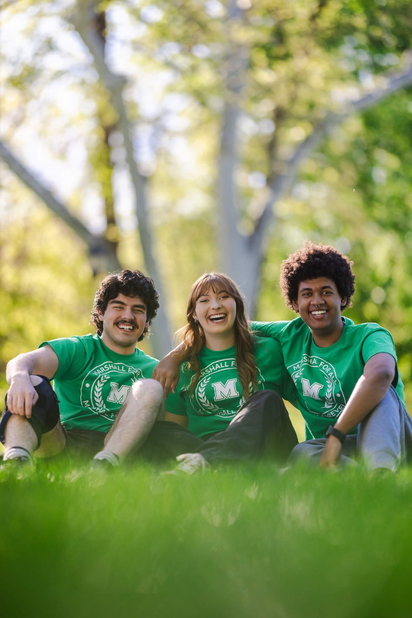 three students smiling at the camera outside in green t-shirts